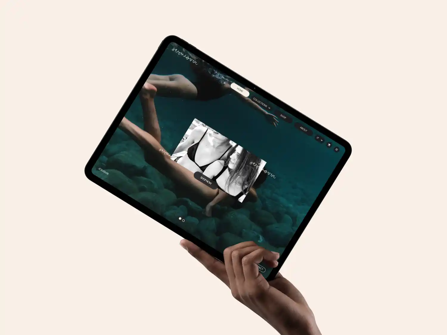 Hand holding a tablet displaying an underwater fashion website with models swimming and a promotional black and white image of a woman in a swimsuit with a 'Shop Now' button.